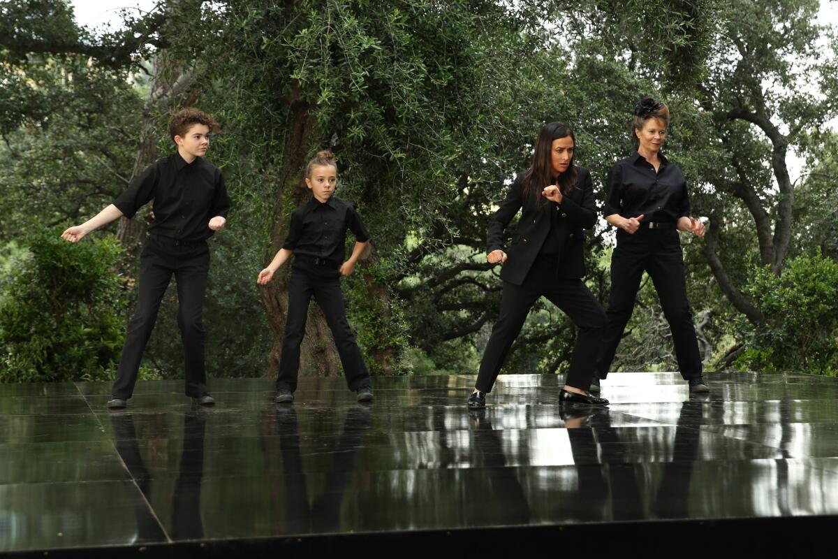 Two girls, their mother and their grandmother, all dressed in black, dancing on a shiny black stage