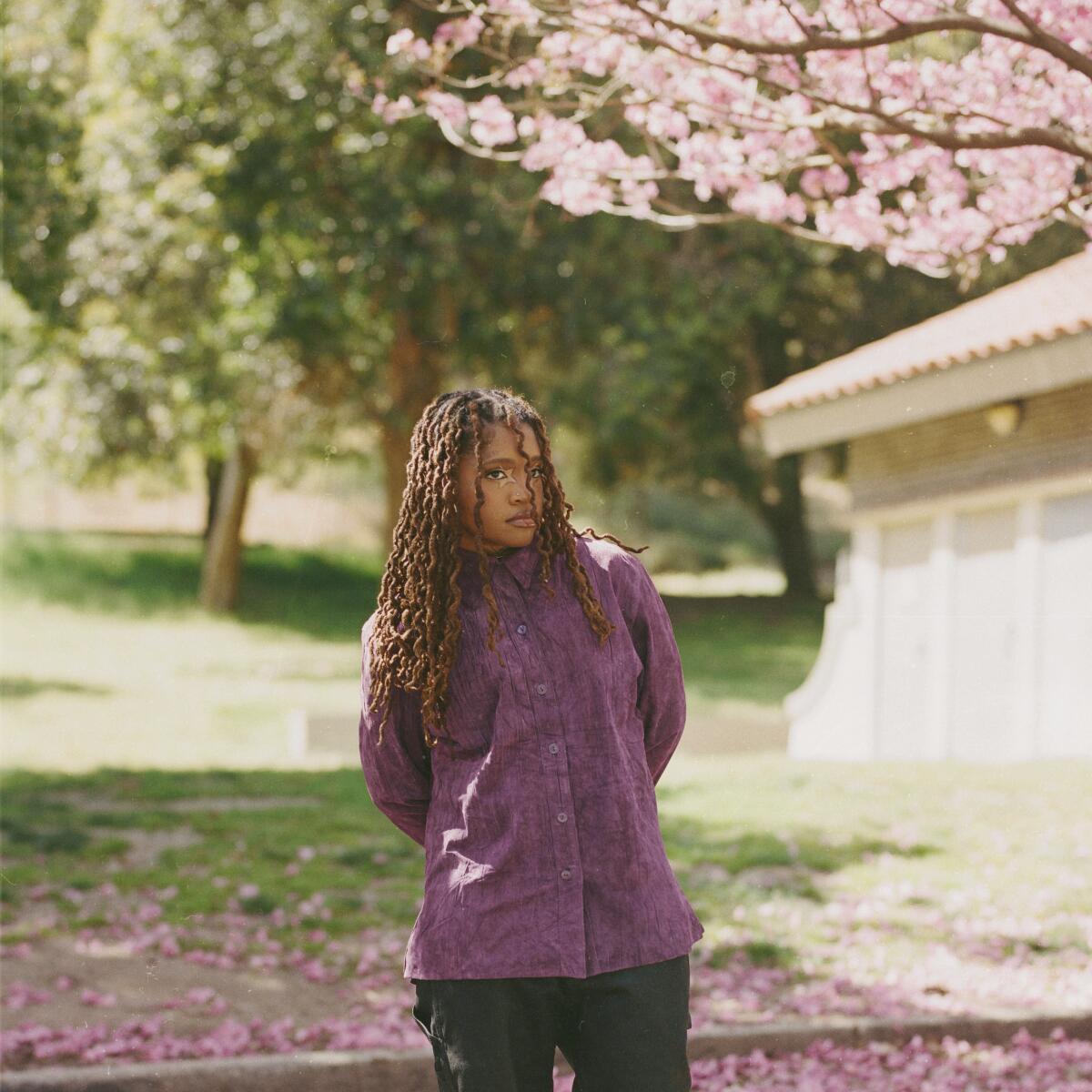 A woman stands under a tree with pink flowers. 