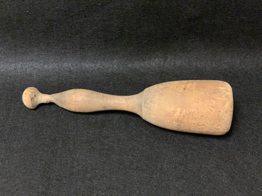 A wooden potato masher rests on its side on a charcoal-colored background.