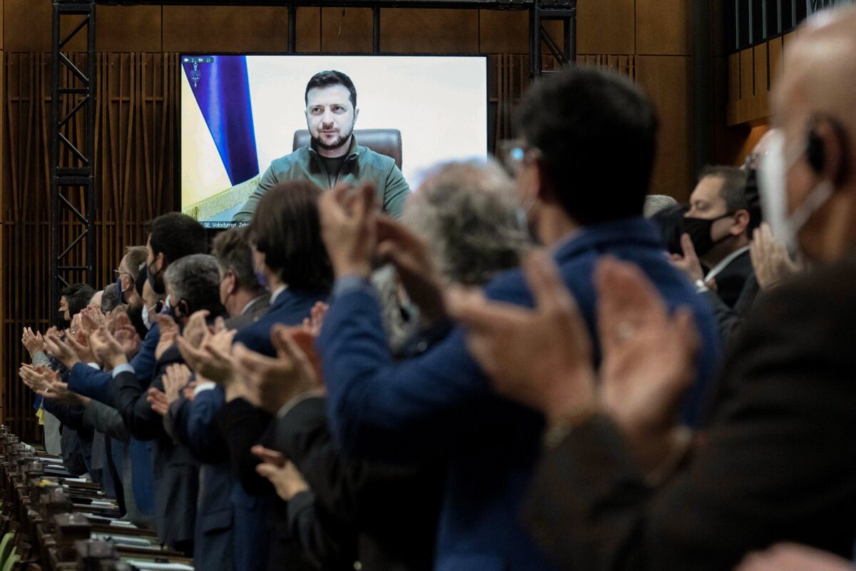 Members of the Canadian Parliament and others applaud as Ukrainian President Volodymyr Zelensky appears on a video screen.