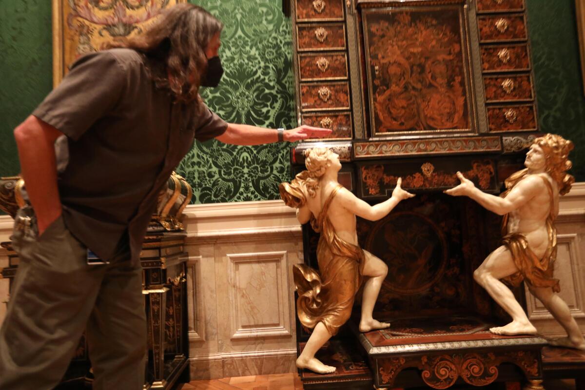 A preparator stands in front of cabinet supported by decorative cherubs. 