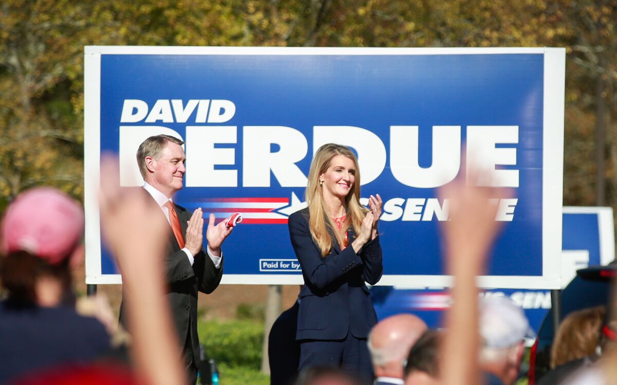 Republican Sens. David Perdue and Kelly Loeffler of Georgia clap in front of a large Perdue campaign sign during a rally.