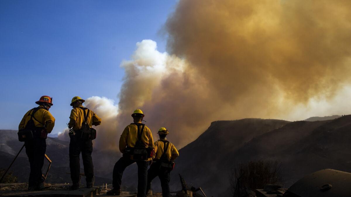 Firefighters watch as a plume of smoke rises from the Woolsey fire near the Chatsworth Reservoir on Sunday.