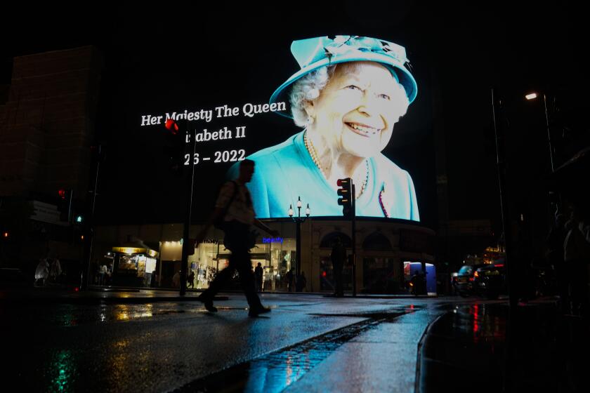 A man walks with an umbrella past an image of Queen Elizabeth II projected onto a large screen at Piccadilly Circus, in London, Thursday, Sept. 8, 2022. Queen Elizabeth II, Britain's longest-reigning monarch and a rock of stability across much of a turbulent century, died Thursday after 70 years on the throne. She was 96. (AP Photo/Alberto Pezzali)