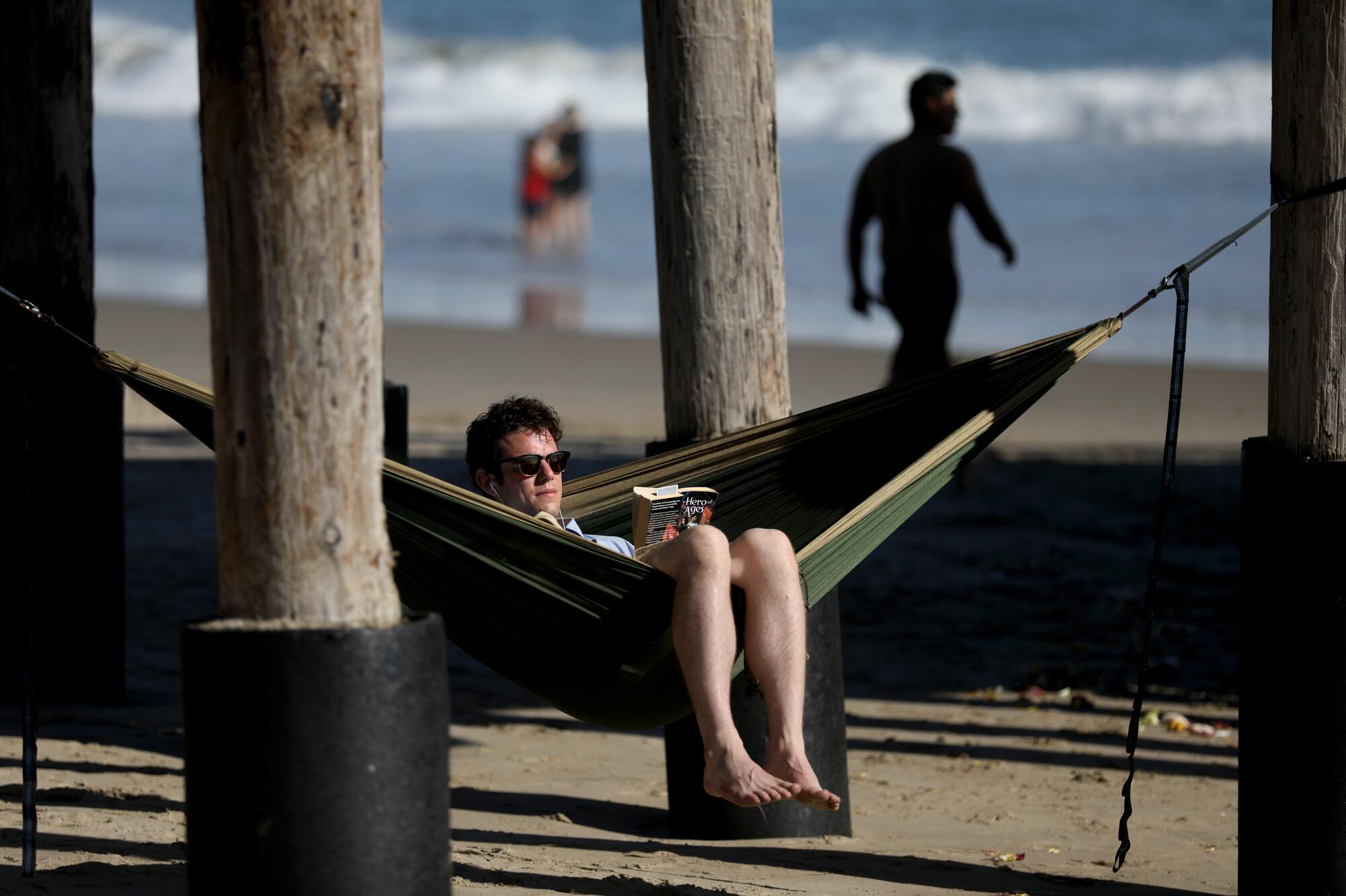 Tyler MacFarland reads a book under the pier at the beach in Ventura. "I am still working, and for the last month and a half it has been just work, home, work, home," he said.