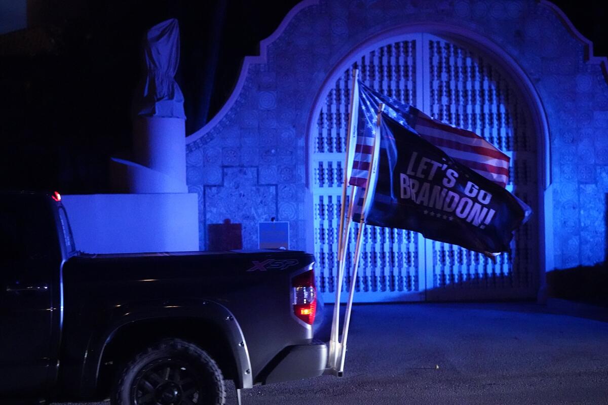 A U.S. flag and one with the words "Let's Go Brandon!" fly from the rear bumper of a truck in front of an ornate doorway