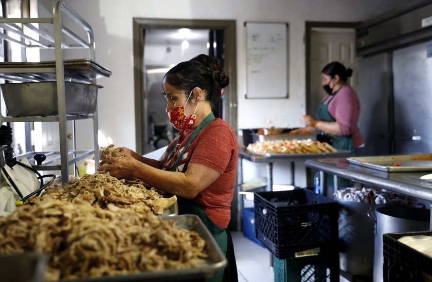 Josefina Pantoja shreds pork as Sylvia Uribe makes tamales at Tamaleria Maria's in Lynwood.