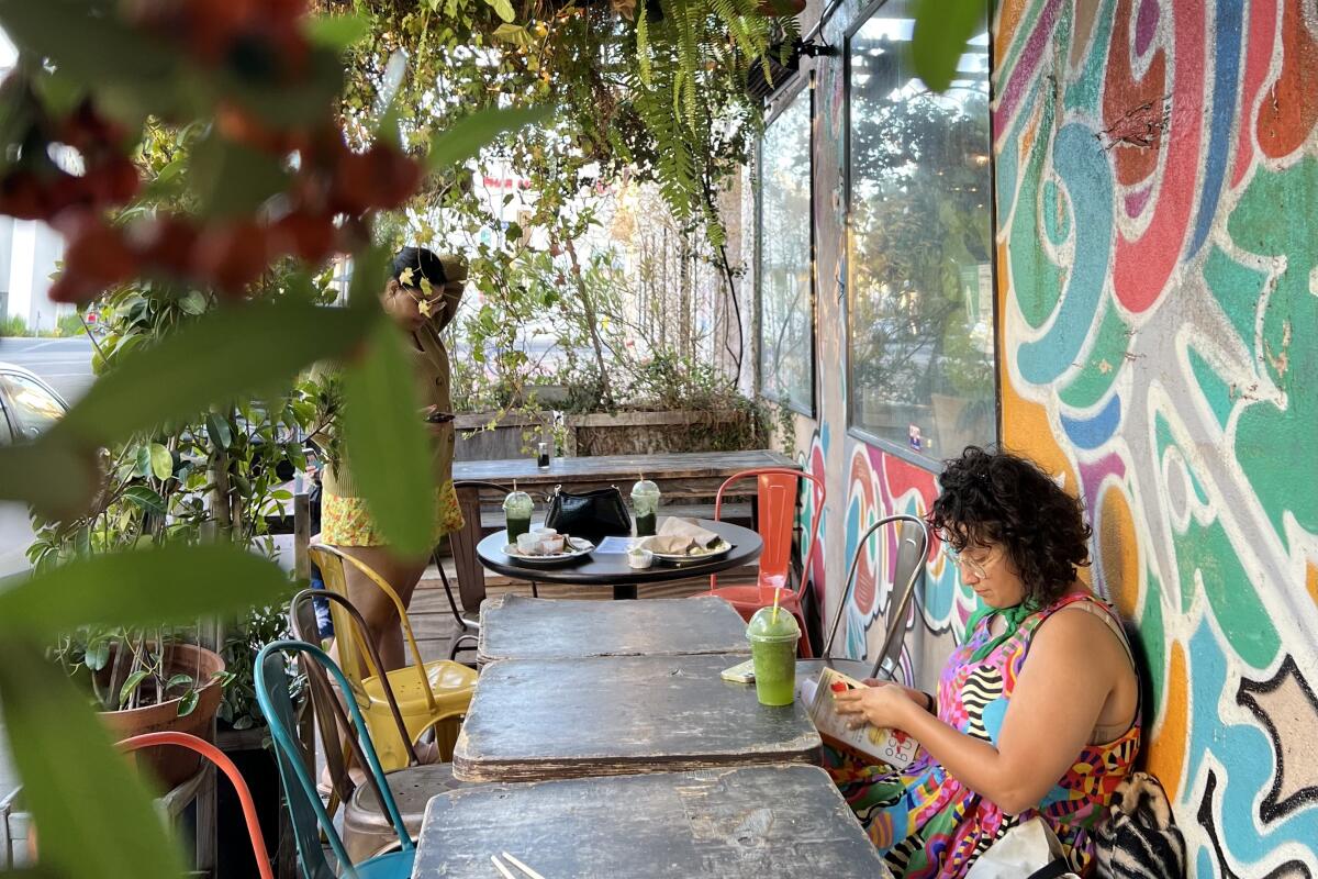 A person sitting at a table in the patio of Yuko Kitchen with a colorful mural on the wall. 