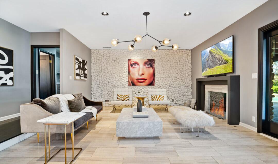 The living room with a chandelier, furniture, fireplace and wall art.
