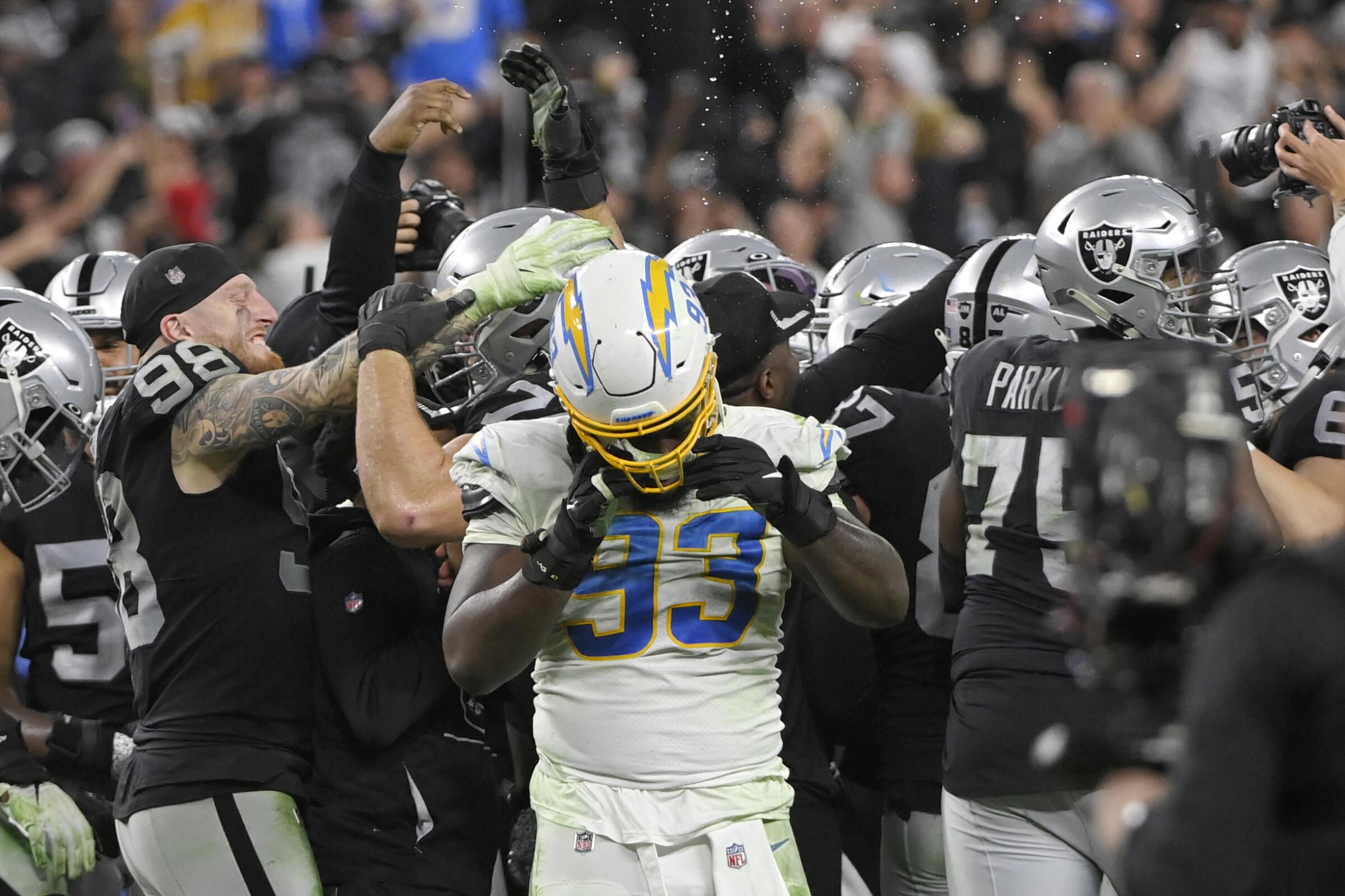 Chargers defensive tackle Justin Jones removes his helmet in front of a group of celebrating Las Vegas Raiders players.
