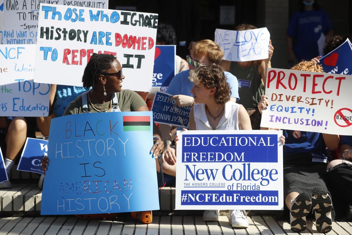 Young people sit on stairs of a building holding handmade signs. One reads "Black history is American History." 