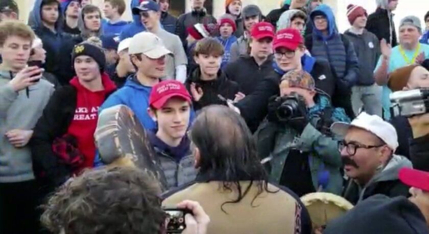 Nicholas Sandmann, center left, stands in front of an Native American Nathan Phillips, who is singing and playing a drum on the steps of the Lincoln Memorial.
