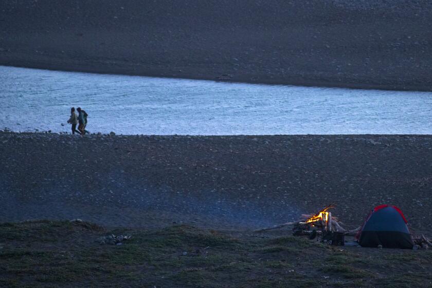 BIG SUR, CA - MAY 01: Beachgoers walk along the shore as a campfire glows on the beach at San Carpoforo Creek on California Highway 1 near Ragged Point on Saturday, May 1, 2021 in Big Sur, CA. (Brian van der Brug / Los Angeles Times)