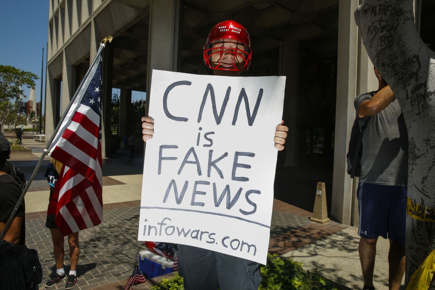 A man holding a sign that says, "CNN is Fake News" and "infowars.com" positioned himself into photos while members of the news media covered the protest march in downtown L.A.