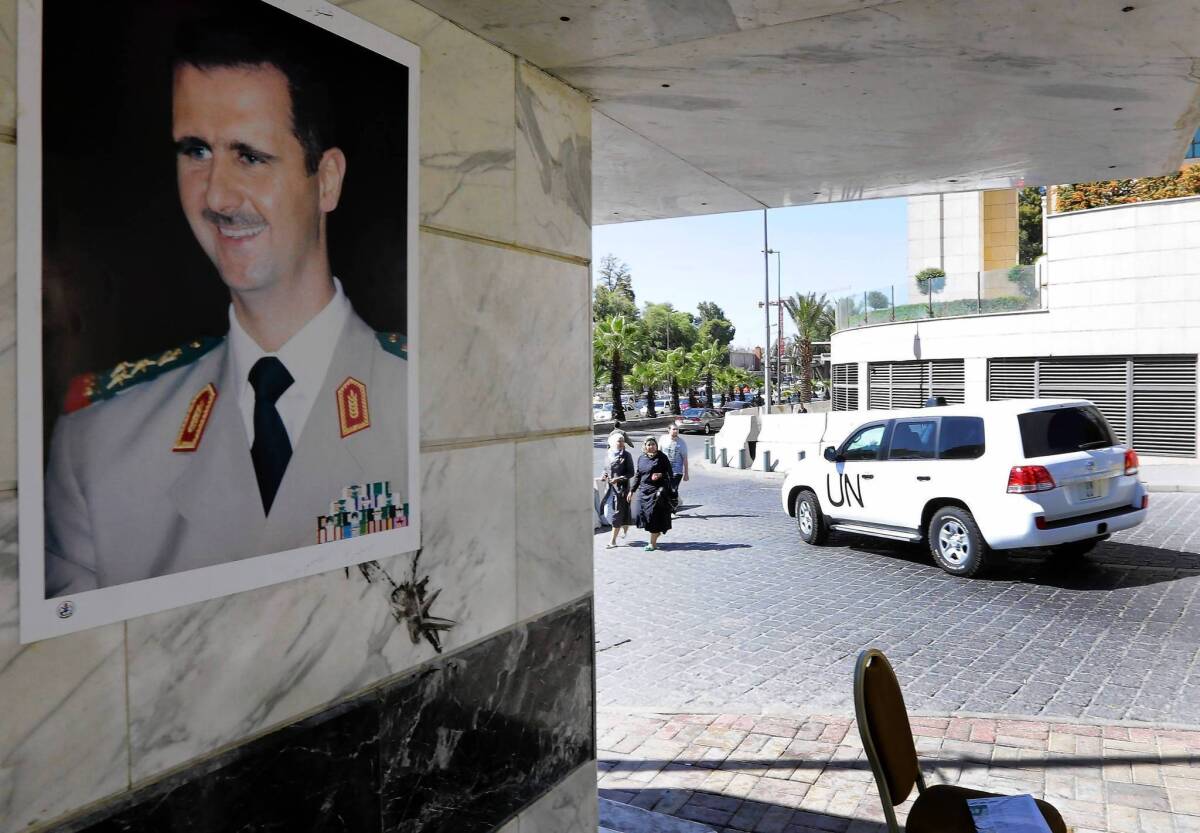 A U.N. vehicle carrying inspectors from the Organization for the Prohibition of Chemical Weapons leaves a hotel in Damascus, where Syrian President Bashar Assad's image adorns a wall.