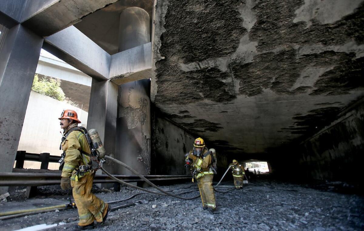 Los Angeles Fire Department firefighters pull hoses out of a freeway tunnel in Los Feliz after a big rig truck and trailer flipped and burned at the transition between the 2 and 5 Freeways on Saturday, July 12, 2013.