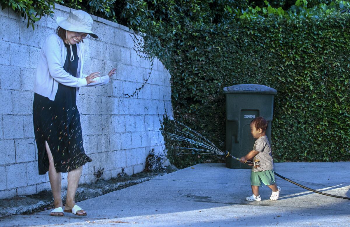 Ian Choi, 21 months old, aims a hose at his mother Younkyung Ko, while playing in front of their home.