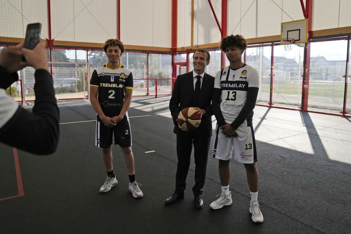 French President Emmanuel Macron poses with youths at a basketball playground in Tremblay-en-France, outside Paris, Thursday, Oct.14, 2021. French President Emmanuel Macron will promote sports ahead of the 2024 Olympic Games in Paris. (AP Photo/Francois Mori, Pool)
