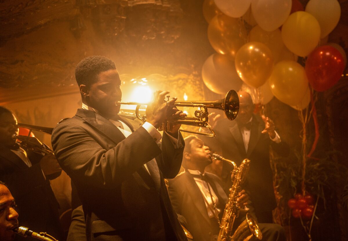A man plays the trumpet at a party with other musicians sitting behind him.