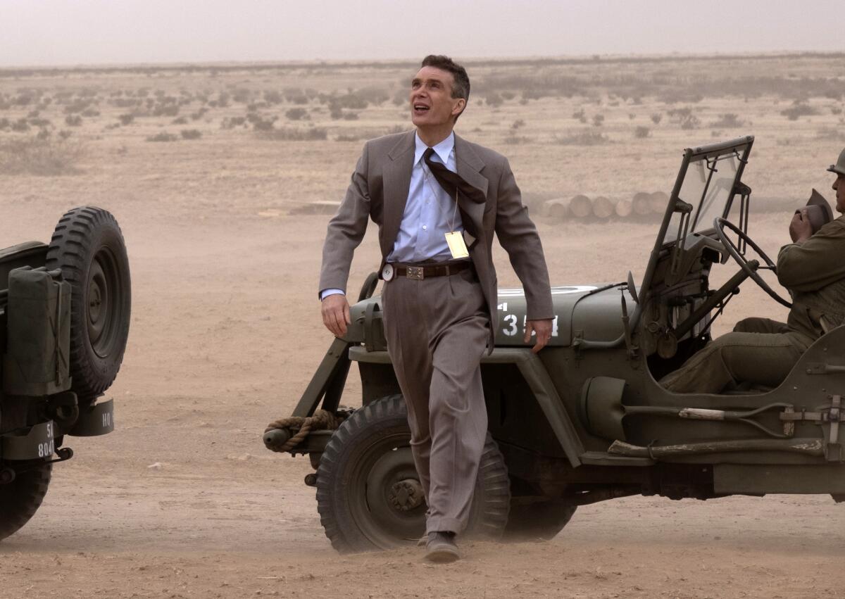 Cillian Murphy, in suit and tie, walks away from a jeep in the desert in a scene from "Oppenheimer."