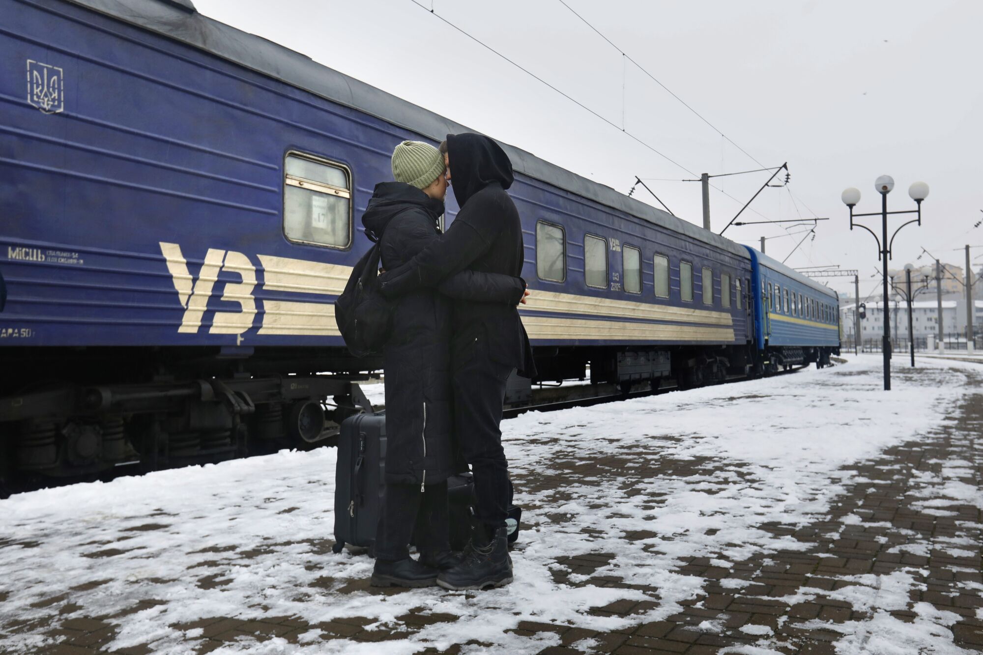 Woman hugs boyfriend at a train platform while snow is on the ground.