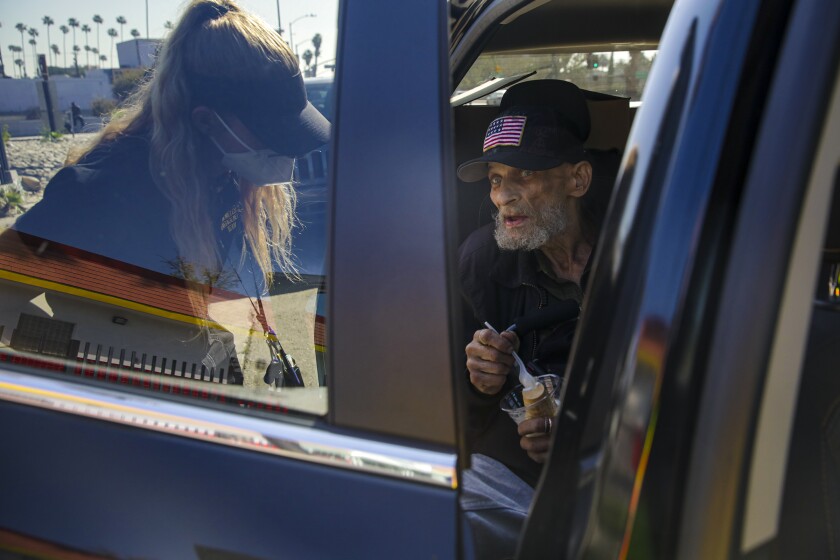 A young woman talks to an older man wearing a ballcap in a vehicle.  
