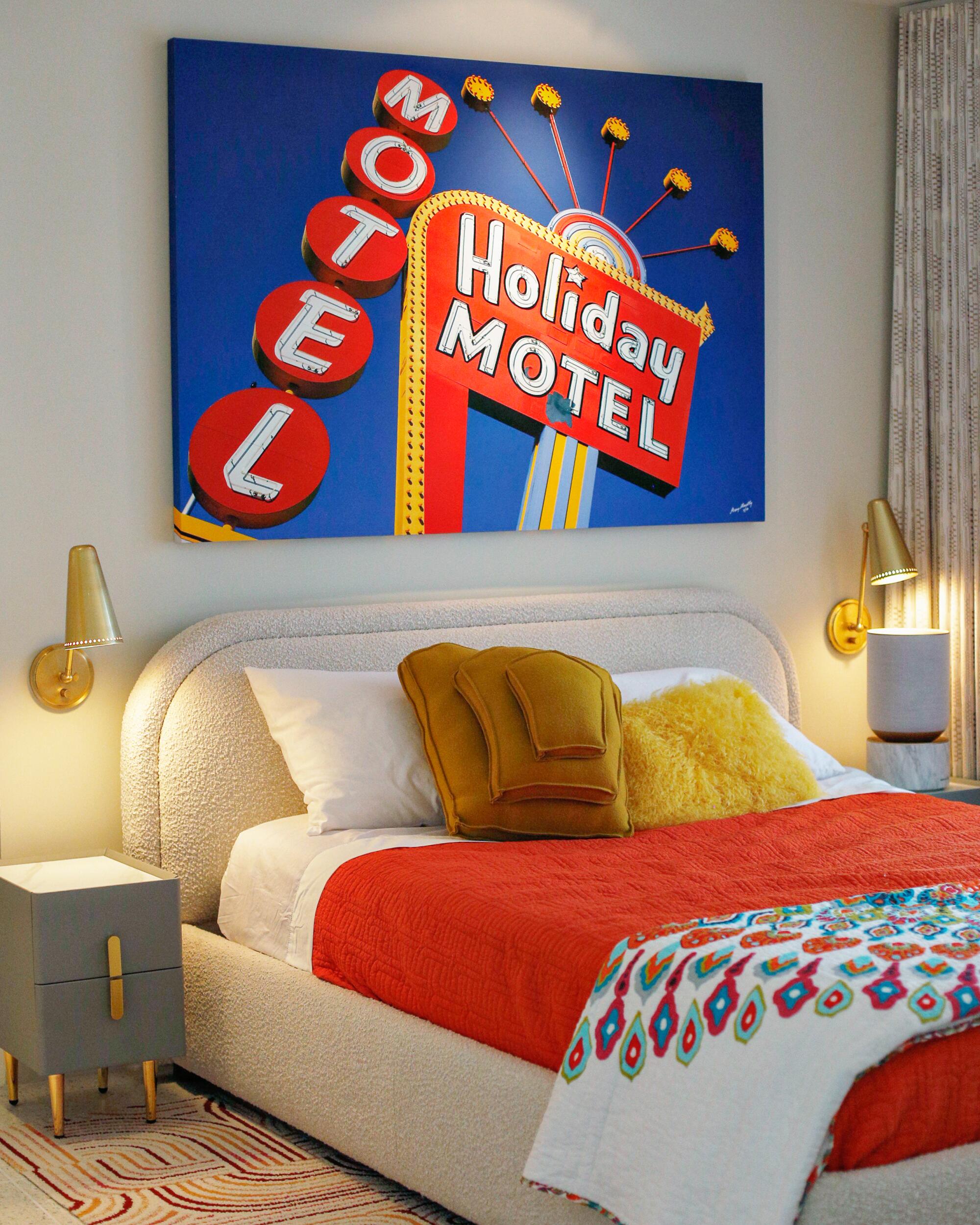 A colorful painting hangs over a bed with a red bedspread