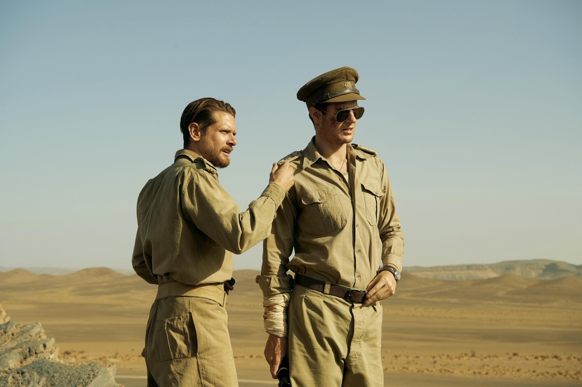Two men in uniform confer in the open desert.
