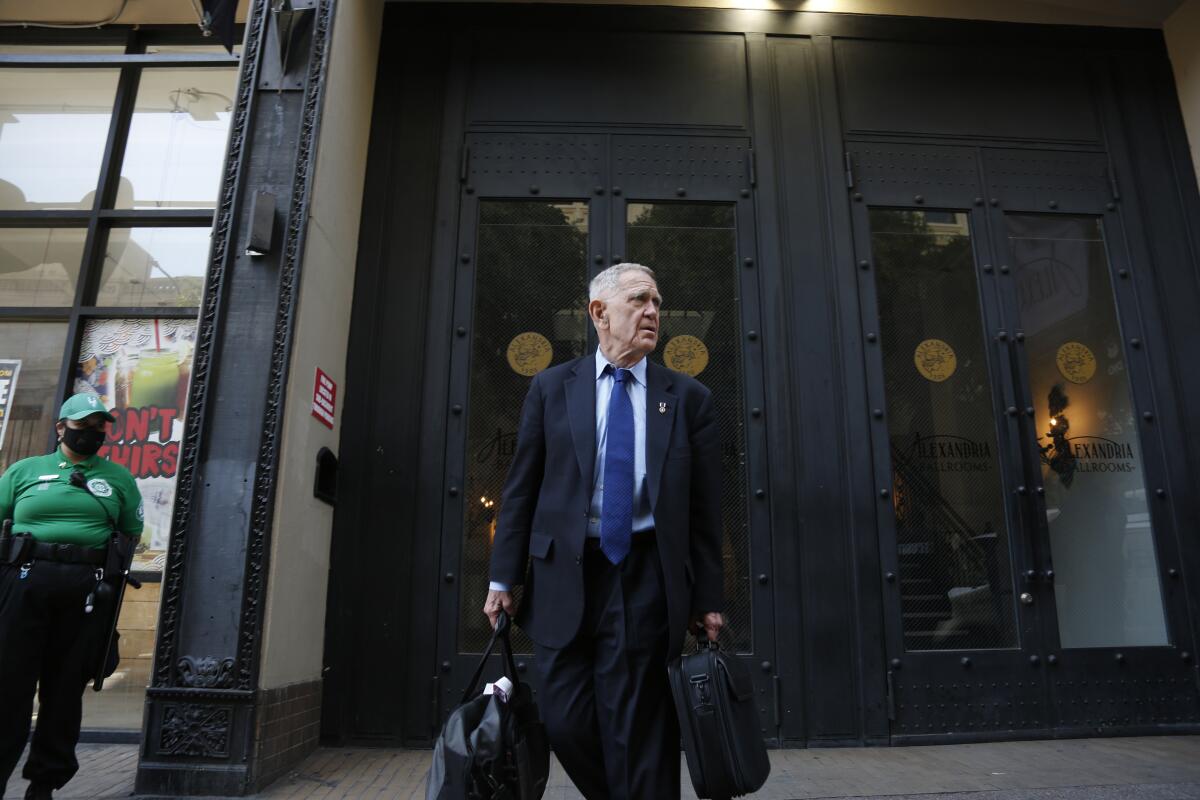 A judge in a suit and tie stands outside a building after presiding over a hearing.