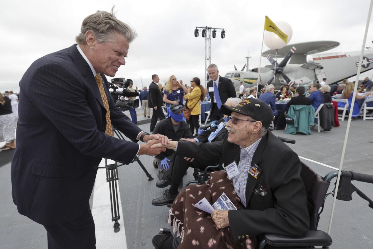 A man stands next to a man in a wheelchair and shakes his hand.