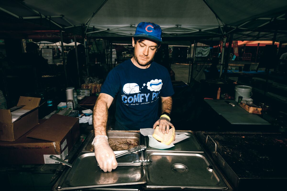 A man puts together a sandwich under a canopy.