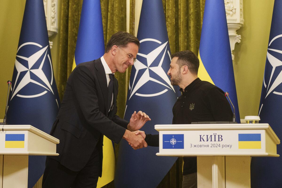 Two men shake hands on a stage in front of NATO and Ukrainian flags