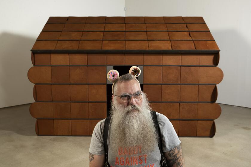 Artist Nayland Blake is photographed next to their piece titled, "Feeder 2," 1998 — a house made out of actual gingerbread. It is on display at the Institute of Contemporary Art Los Angeles, part of the artist's most comprehensive retrospective to date, "No Wrong Holes: Thirty Years of Nayland Blake." The artist uses they/their as a gender pronoun.