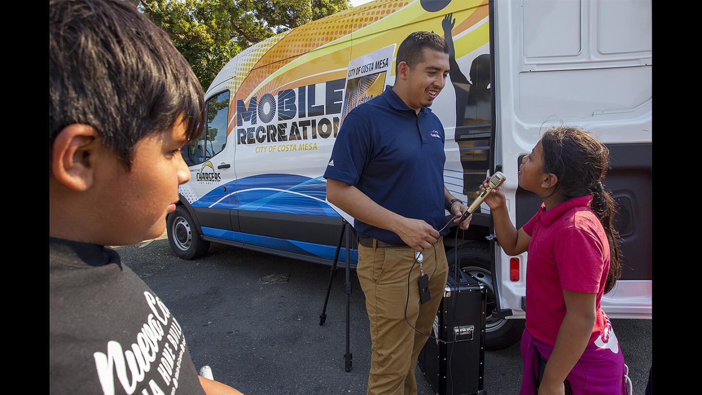 Christian Hernadez, assistant recreation supervisor for the city of Costa Mesa, helps Maria Leon, 10, with a karaoke machine on Monday. Costa Mesa is bringing back its mobile recreation program, which includes a van stocked with games, crafts and sports equipment.