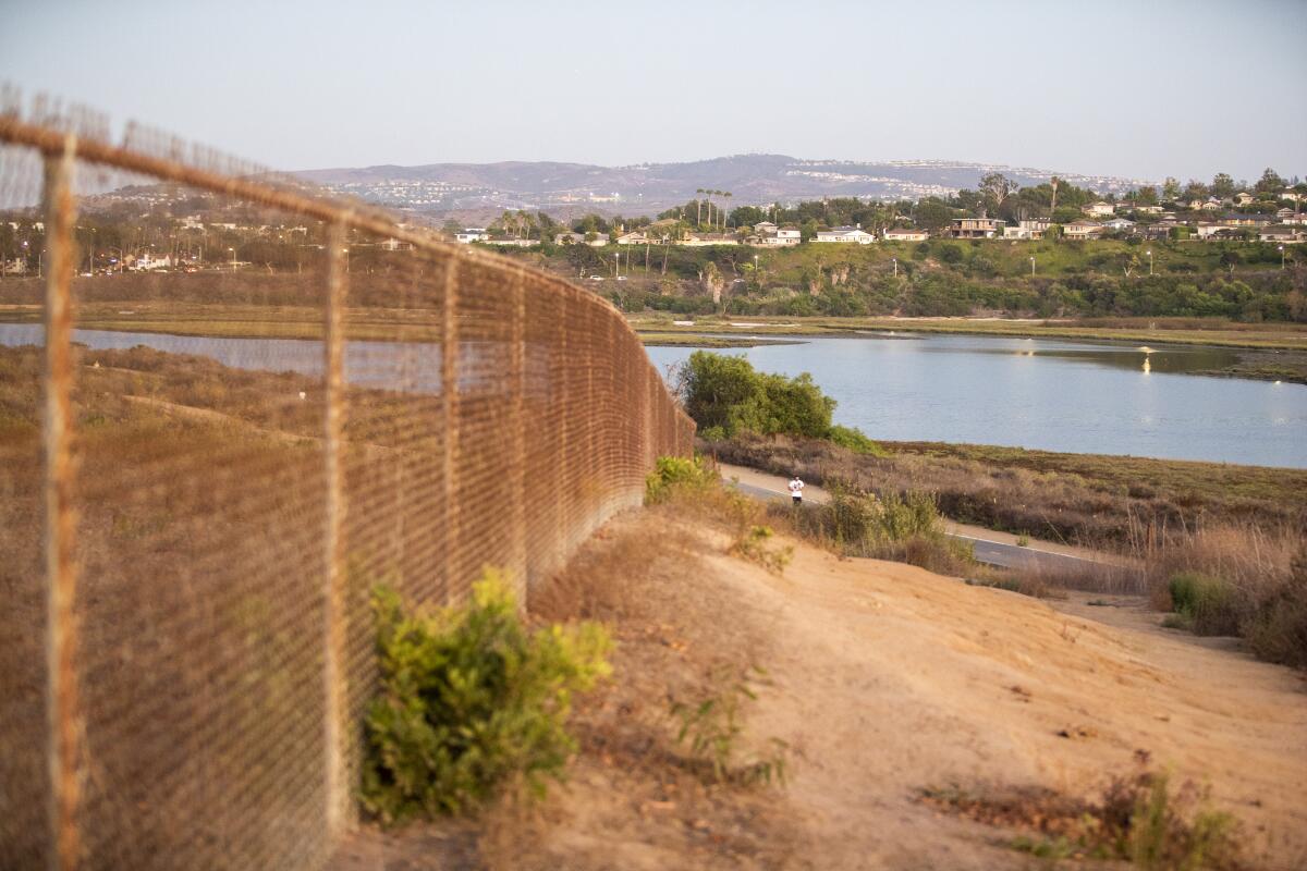 A fence runs along a hillside toward a body of water.
