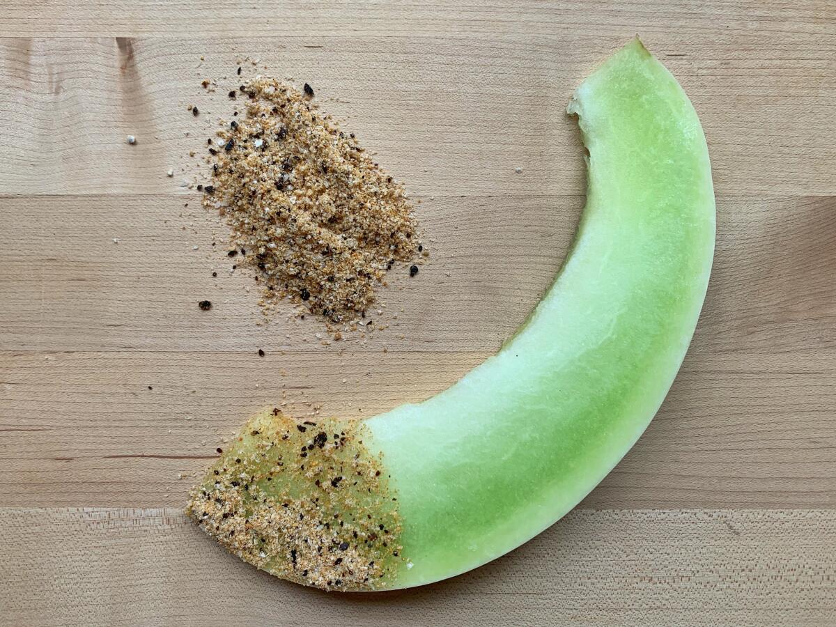 A slice of green melon, one end dipped in a seed and spice salt blend