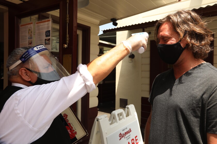 Waiter Pedro Armenta, wearing a face shield and mask, checks the temperature of customer Julian Bourely before entering Dupar's Restaurant - California coronavirus