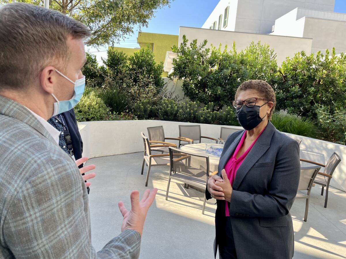 People with face masks on stand and talk in an outdoor seating area.