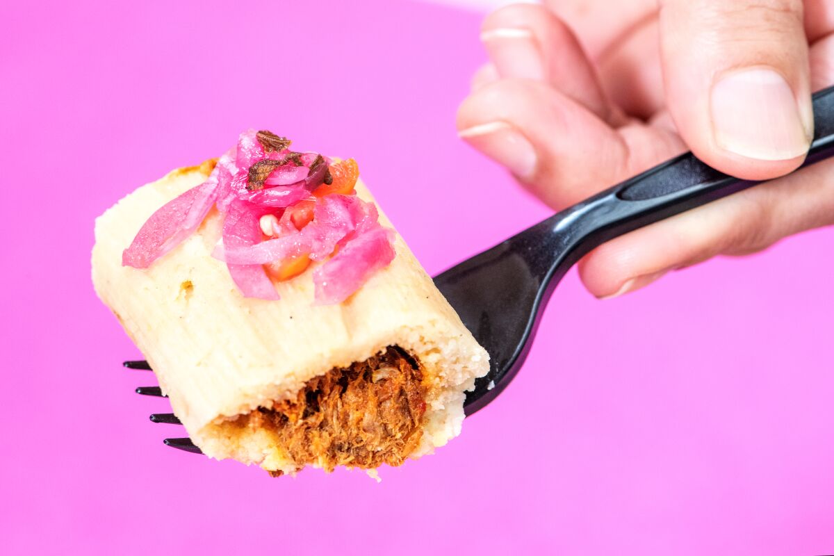 A bite of the braised pork tamale from Artesano Tamaleria on a black fork against a pink background.