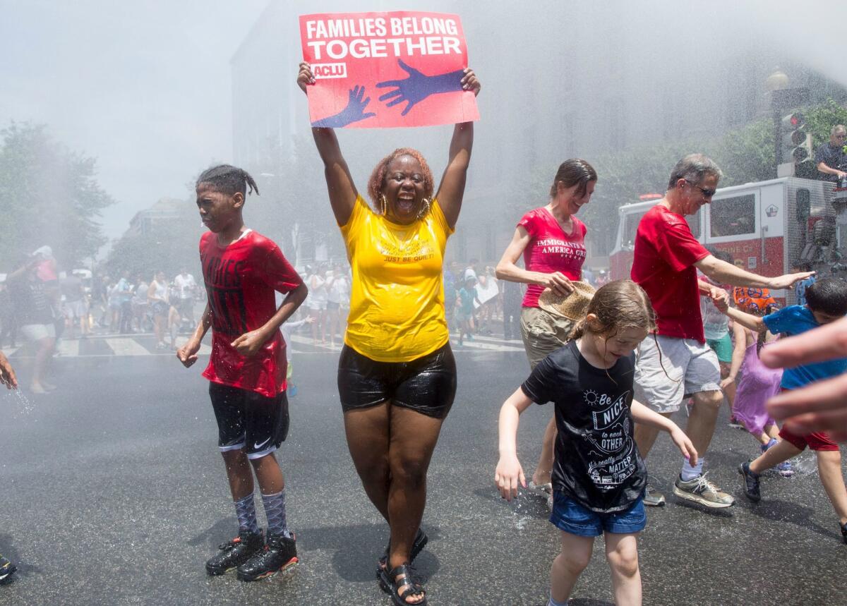 WASHINGTON, D.C.: A woman holds a sign while joining others underneath water being sprayed by a firetruck to cool off people attending a Families Belong Together rally.