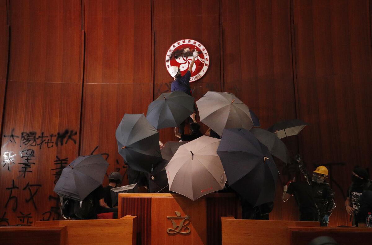 Protesters with umbrellas paint graffiti in a council chamber. 
