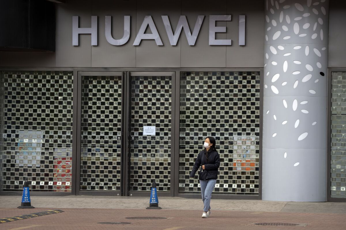 A woman wearing a face mask walks past a Huawei store temporarily closed due to coronavirus-related restrictions in Beijing, Thursday, May 12, 2022. China's leaders are struggling to reverse a deepening economic slump while keeping a "zero-COVID" strategy that has shut down Shanghai and other cities. (AP Photo/Mark Schiefelbein)