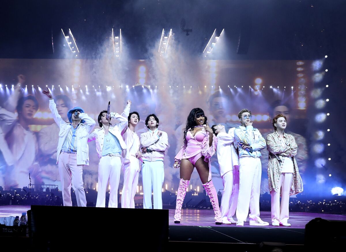 A woman in a pink costume holding a microphone standing in the middle of a group of seven men on a stage
