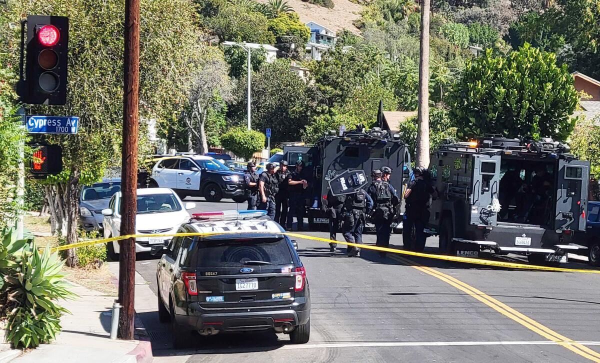 Police cruisers and SWAT armored vehicles on a residential street behind yellow police tape