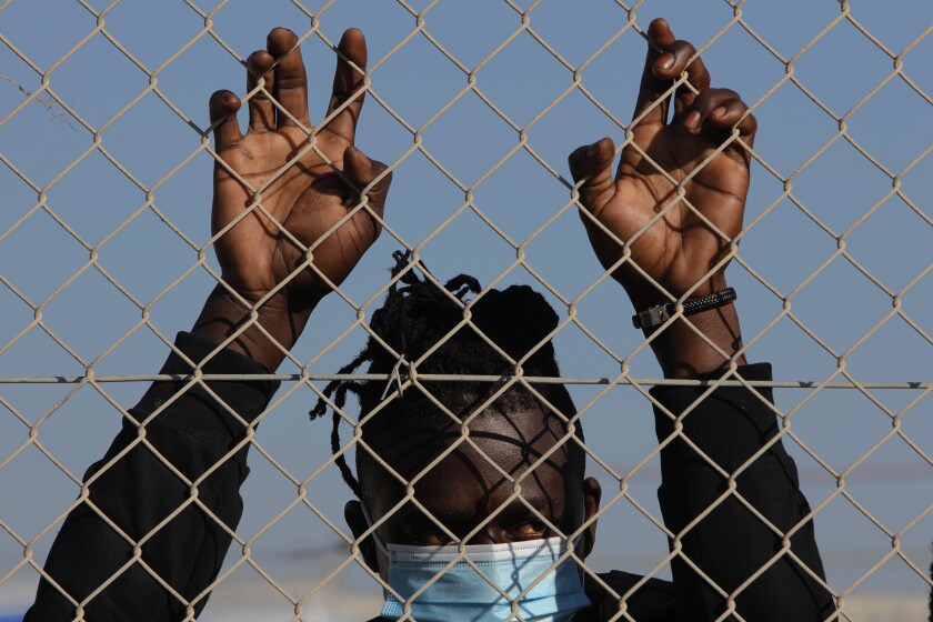 A migrant wearing a face mask stands behind a fence inside a refugee camp in Kokkinotrimithia outside of capital Nicosia, Cyprus, Friday, Feb. 5, 2021. Cyprus' Interior Minister Nicos Nouris said this week that the east Mediterranean island nation whose closest point to Syria is around 150 kilometers (93 miles) remains first among all other European Union member states with the most asylum applications relative to its population. Last year, the country of around 1.1 million people racked up 7,000 asylum applications - most of them from Syrians (AP Photo/Petros Karadjias)