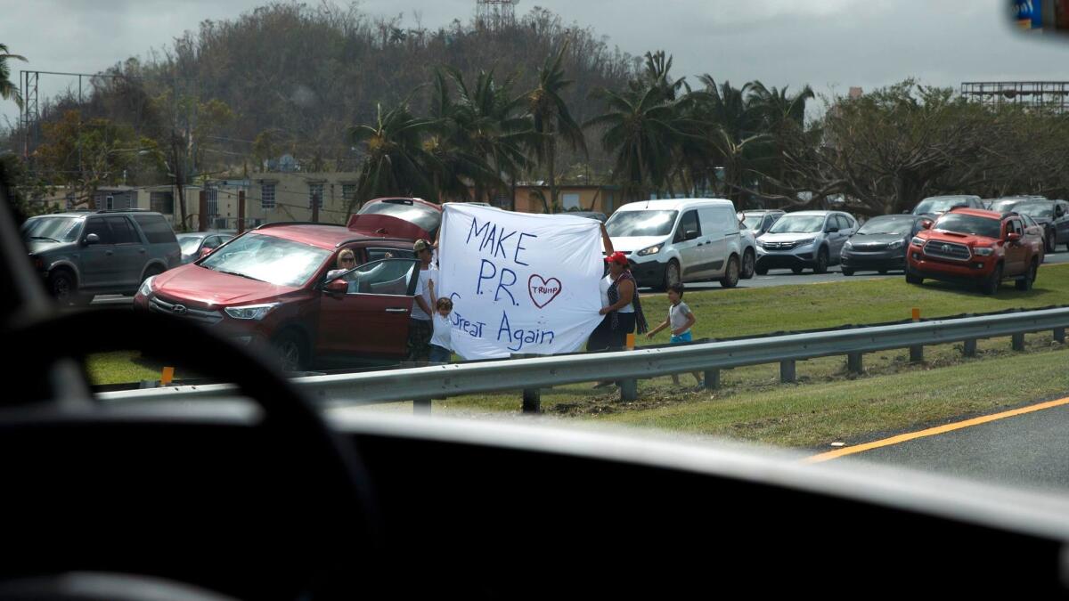 People hold a sign as President Trump's motorcade passes by in Guaynabo, Puerto Rico.