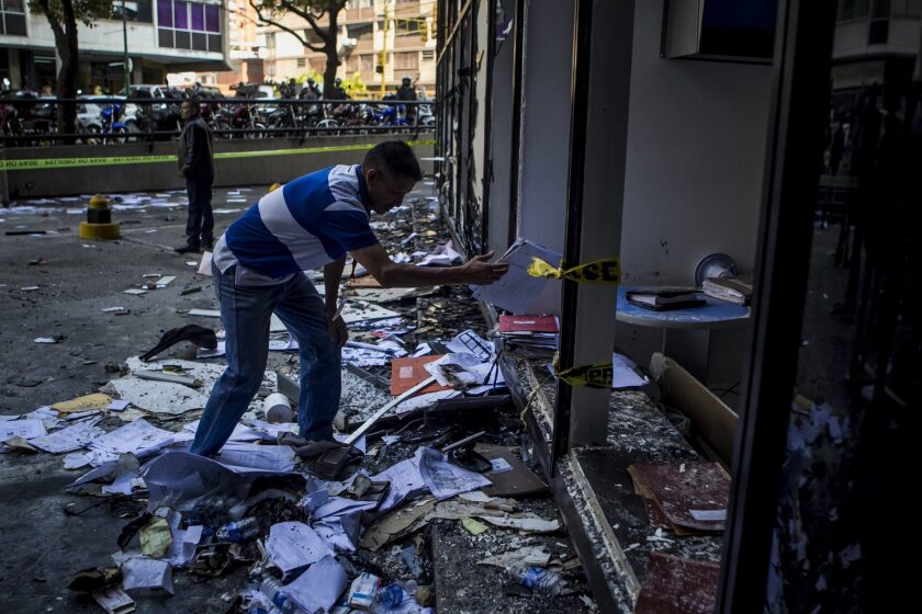 A man removes broken glass outside an office in Caracas, Venezuela, that was damaged during demonstrations against the government of President Nicolas Maduro.