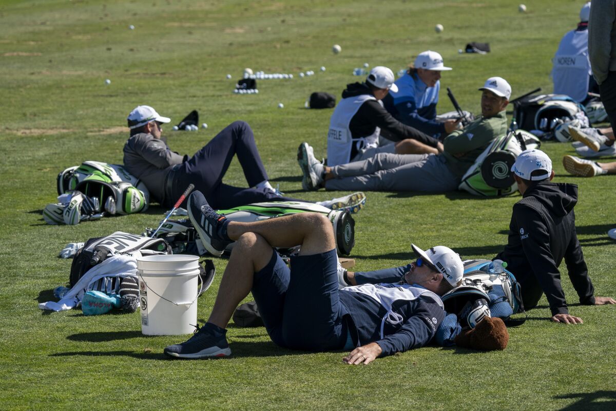 Golfers and caddies wait out a wind delay on the practice range during the third round of the Genesis Invitational.