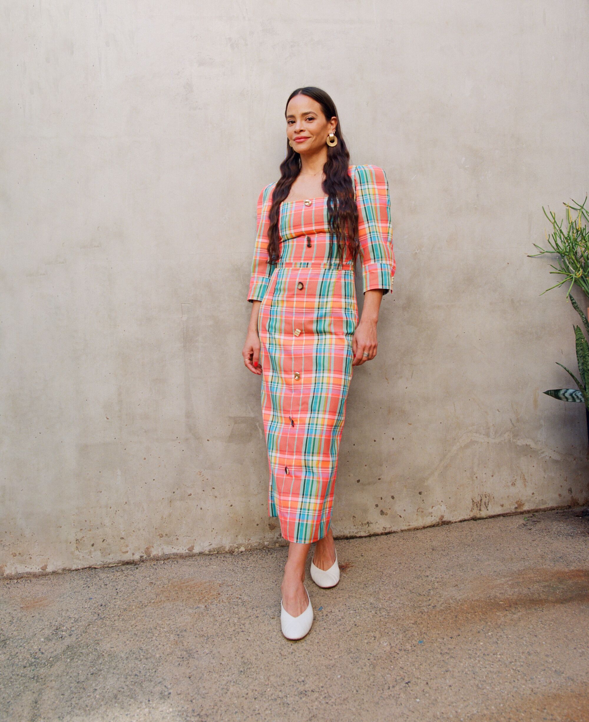 A woman with long dark hair, standing, wearing a colorful pastel dress.