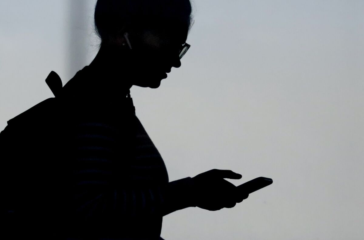 A silhouette of a woman wearing glasses and her hair up checking her phone.
